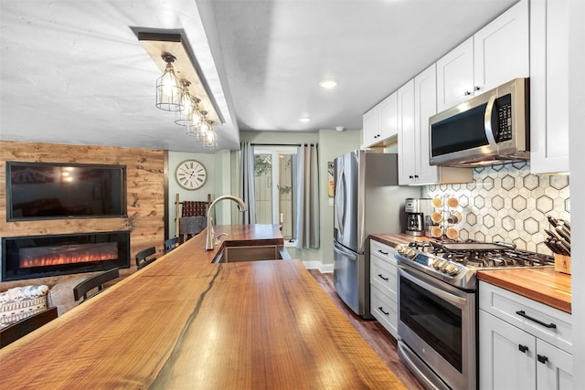 kitchen with wooden counters, appliances with stainless steel finishes, white cabinets, and decorative light fixtures