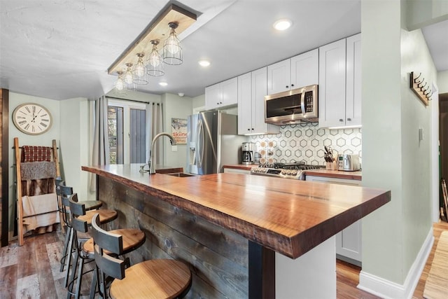 kitchen featuring a center island with sink, white cabinets, butcher block counters, and appliances with stainless steel finishes