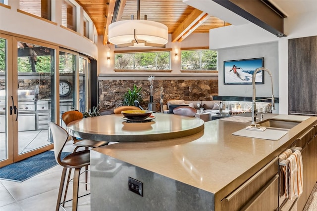 kitchen with wooden ceiling, sink, light tile patterned floors, an island with sink, and beam ceiling