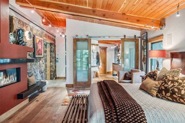 bedroom with rail lighting, wood ceiling, a barn door, light hardwood / wood-style flooring, and vaulted ceiling with beams