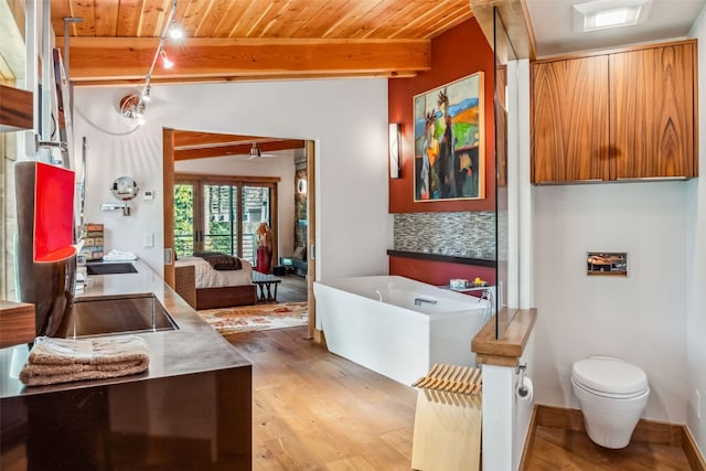 bathroom with a bathtub, rail lighting, vaulted ceiling with beams, toilet, and wood-type flooring