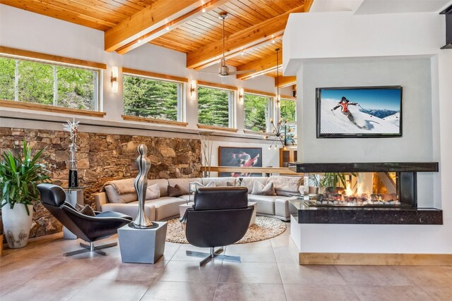 living room with a wealth of natural light, beam ceiling, a multi sided fireplace, and a high ceiling