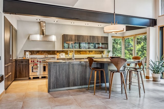 kitchen with pendant lighting, range with two ovens, wall chimney range hood, a kitchen bar, and kitchen peninsula