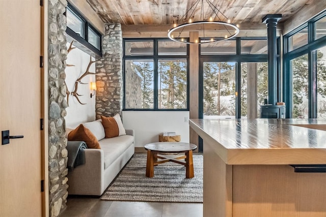 sunroom featuring an inviting chandelier, a healthy amount of sunlight, a wood stove, and wooden ceiling