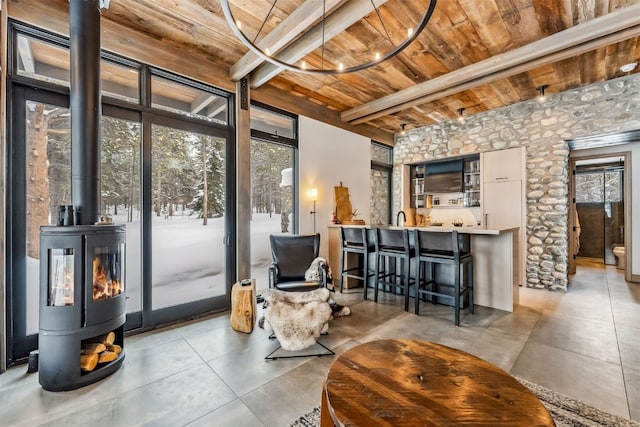 living area featuring a wood stove, sink, beam ceiling, and wood ceiling