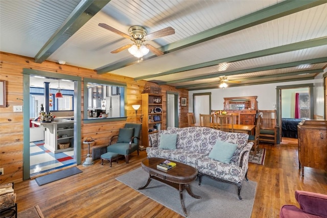 living area with beamed ceiling, wood finished floors, wood walls, and ceiling fan