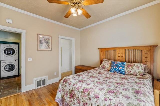 bedroom with stacked washer / dryer, visible vents, baseboards, hardwood / wood-style floors, and ornamental molding