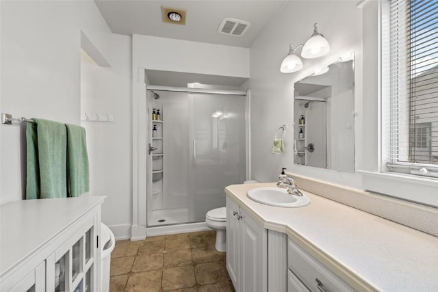 bathroom with vanity, a shower stall, toilet, and visible vents