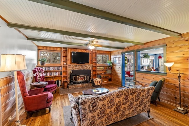 living area featuring beam ceiling, wood walls, a wood stove, and hardwood / wood-style flooring