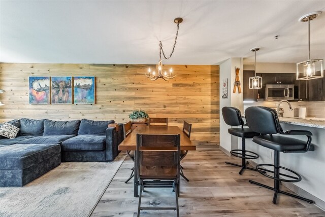 dining area with wood walls, an inviting chandelier, and light hardwood / wood-style flooring