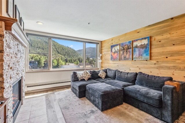 living room featuring a mountain view, a baseboard radiator, a stone fireplace, and wooden walls