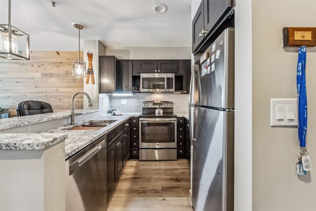 kitchen with light stone counters, stainless steel appliances, sink, pendant lighting, and hardwood / wood-style flooring