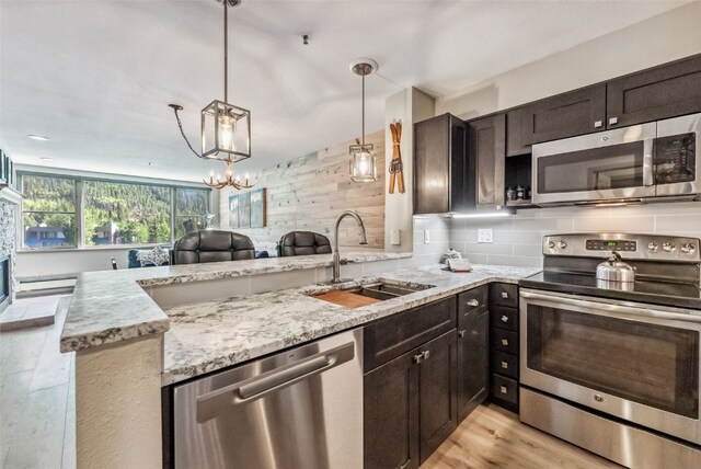 kitchen featuring kitchen peninsula, stainless steel appliances, sink, pendant lighting, and wood walls