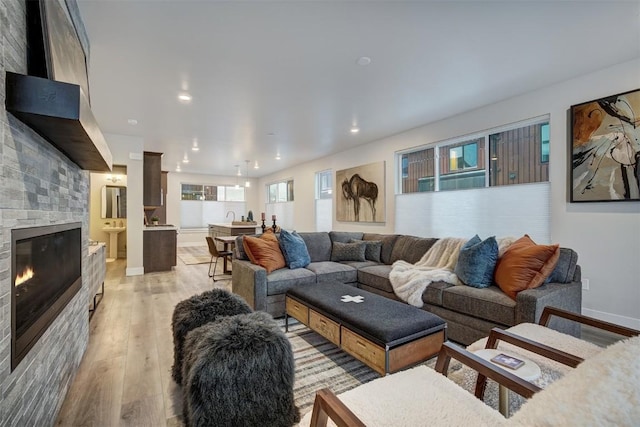 living room with a stone fireplace, light wood-style flooring, recessed lighting, and baseboards