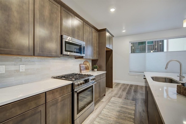 kitchen with light stone countertops, a sink, appliances with stainless steel finishes, light wood-type flooring, and backsplash