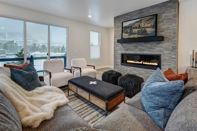 living area featuring a stone fireplace, plenty of natural light, wood finished floors, and baseboards