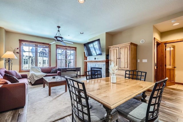 dining space with a tile fireplace, a textured ceiling, ceiling fan, and light hardwood / wood-style flooring