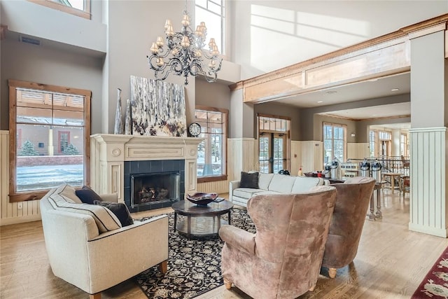 living room featuring an inviting chandelier, a tile fireplace, light hardwood / wood-style floors, and a high ceiling