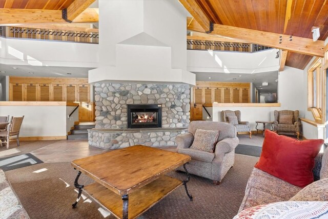 living room with beamed ceiling, a stone fireplace, wooden ceiling, and high vaulted ceiling