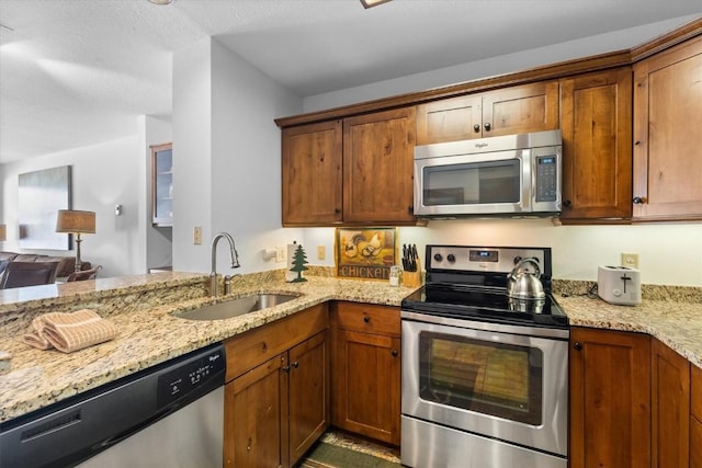 kitchen with stainless steel appliances, light stone countertops, sink, and kitchen peninsula