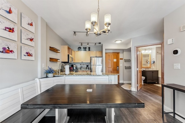 unfurnished dining area featuring baseboards, dark wood finished floors, an inviting chandelier, a sink, and rail lighting