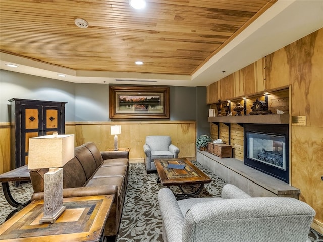 carpeted living room with a raised ceiling, wooden walls, wood ceiling, and wainscoting