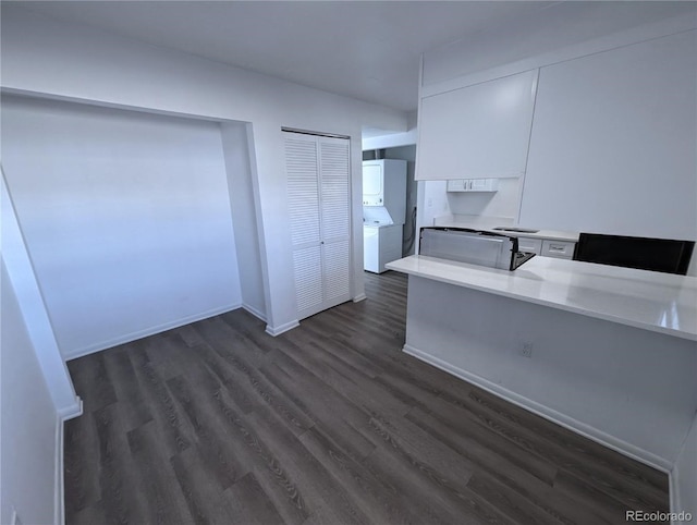 kitchen featuring stacked washer / dryer, white cabinetry, kitchen peninsula, and dark wood-type flooring