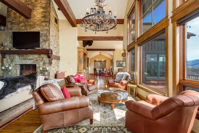 living room featuring beam ceiling, a stone fireplace, wood-type flooring, and an inviting chandelier