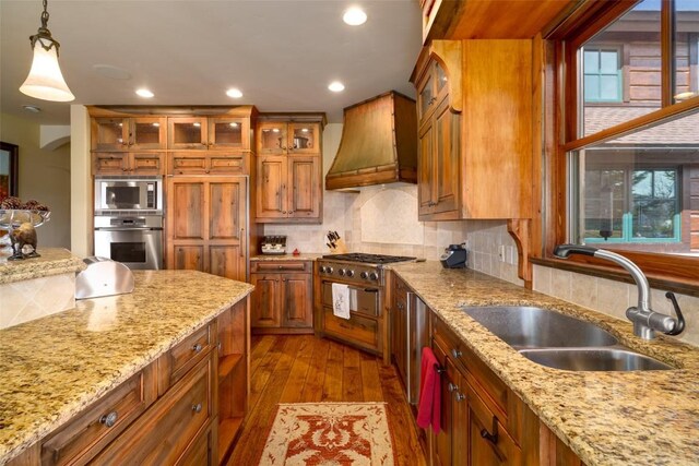 kitchen with appliances with stainless steel finishes, custom exhaust hood, dark wood-type flooring, sink, and decorative light fixtures