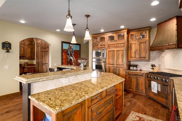 kitchen with dark wood-type flooring, premium range hood, decorative light fixtures, a kitchen island, and appliances with stainless steel finishes