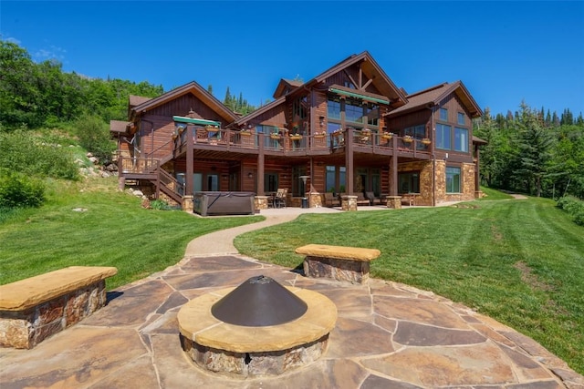 back of property featuring a wooden deck, an outdoor fire pit, a patio, a hot tub, and a lawn