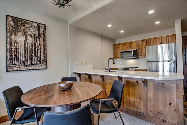 kitchen featuring sink, appliances with stainless steel finishes, a kitchen bar, light colored carpet, and kitchen peninsula