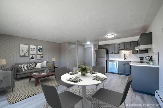 dining room featuring sink, a baseboard heating unit, light wood-type flooring, and a textured ceiling