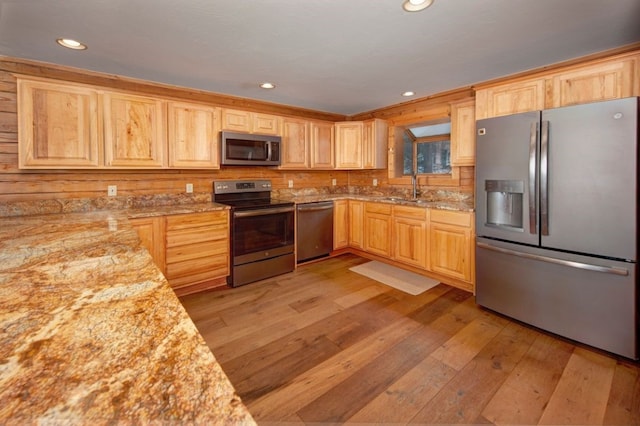 kitchen with appliances with stainless steel finishes, light brown cabinetry, sink, light stone counters, and light wood-type flooring