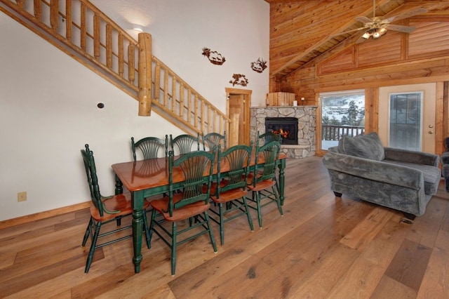 dining room with ceiling fan, a towering ceiling, a fireplace, light wood-type flooring, and wood walls