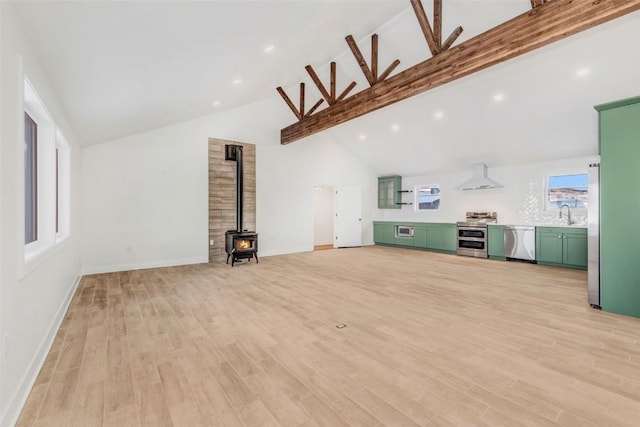 unfurnished living room with light wood-type flooring, lofted ceiling with beams, a wood stove, and sink