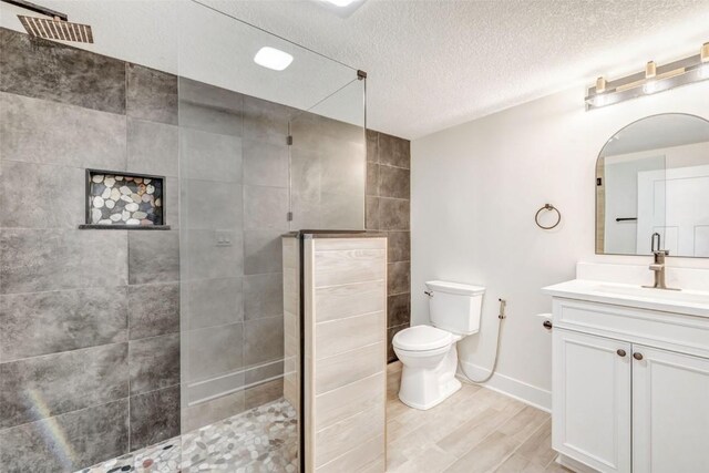 bathroom featuring tiled shower, a textured ceiling, vanity, and toilet