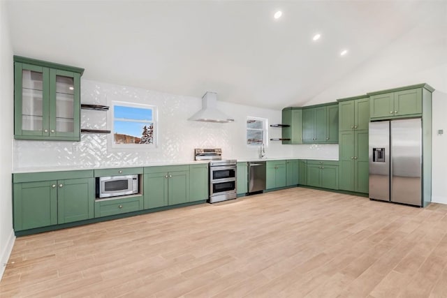 kitchen with light hardwood / wood-style floors, stainless steel appliances, wall chimney range hood, and green cabinetry