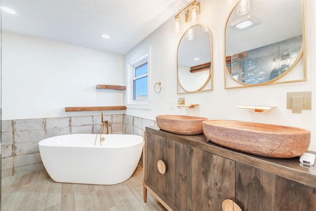 bathroom with vanity, a tub to relax in, and tile walls