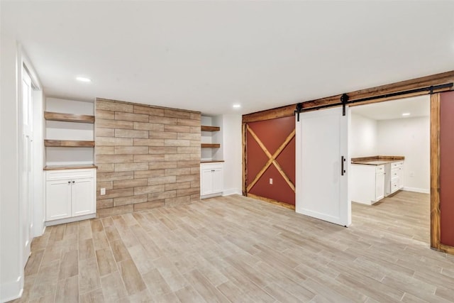 unfurnished living room with a barn door and light wood-type flooring