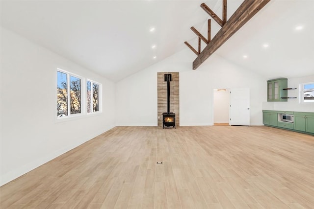 unfurnished living room with lofted ceiling with beams, light hardwood / wood-style floors, and a wood stove