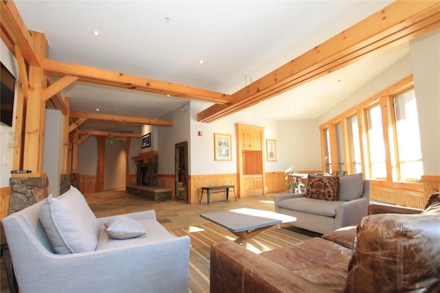 living area with a fireplace with raised hearth, wood walls, wainscoting, and beam ceiling