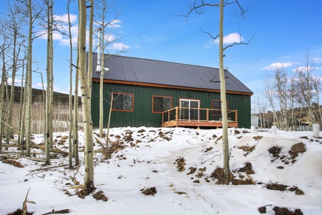 snow covered back of property with metal roof and a wooden deck