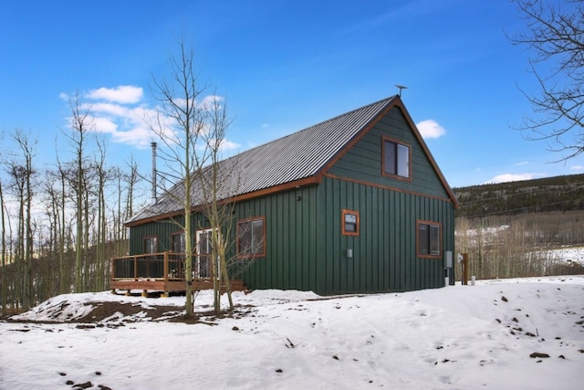 snow covered rear of property featuring board and batten siding, metal roof, a detached garage, and a wooden deck