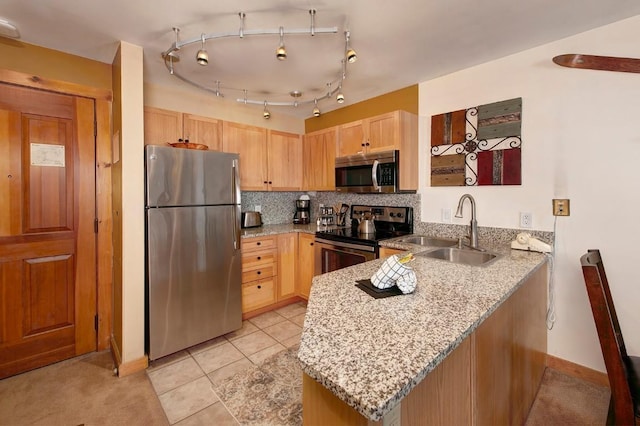 kitchen featuring stainless steel appliances, decorative backsplash, light brown cabinets, a sink, and a peninsula