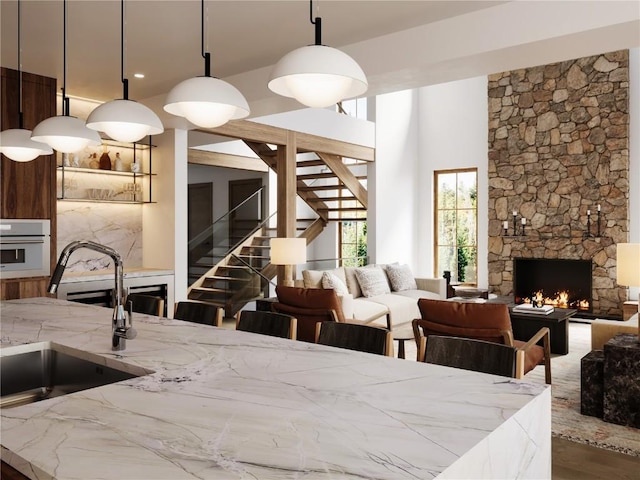 kitchen featuring light stone counters, white oven, open floor plan, a sink, and a stone fireplace