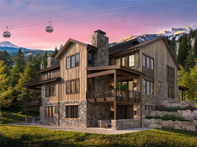 exterior space featuring stone siding, a mountain view, a chimney, and a balcony