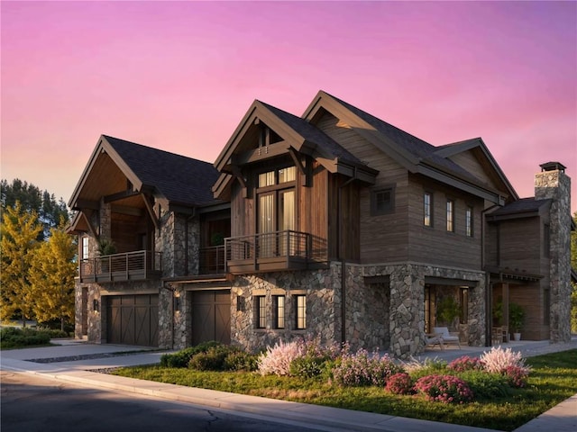 view of front of home featuring driveway, a balcony, stone siding, a chimney, and an attached garage