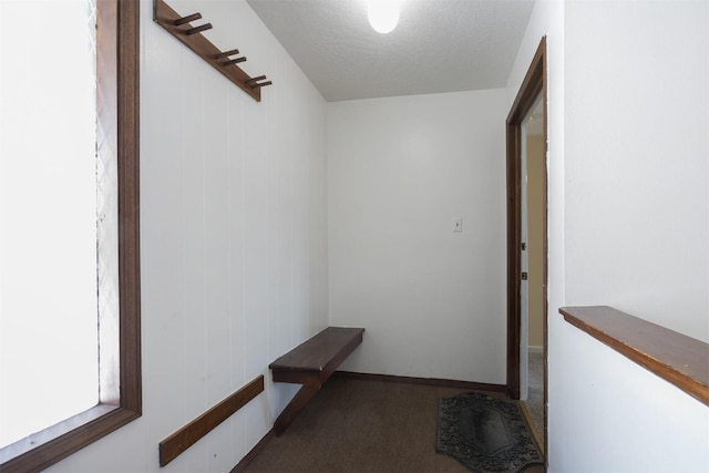 hall featuring a textured ceiling and dark colored carpet