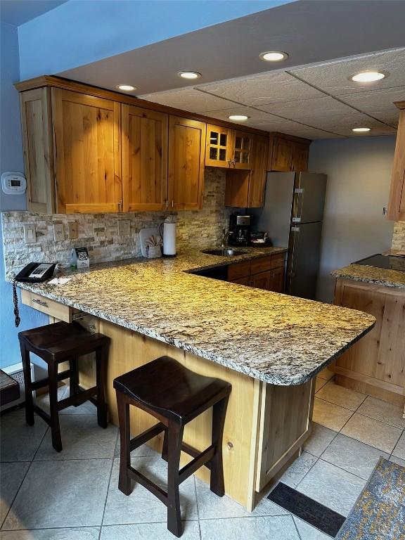 kitchen with kitchen peninsula, a kitchen breakfast bar, stainless steel fridge, backsplash, and light stone counters